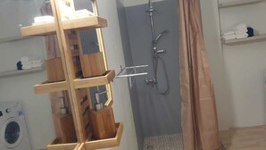 Une salle de bain avec une douche, une étagère en bois et un lave-linge.