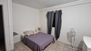 Une chambre à coucher avec un lit, une table de chevet, un ventilateur et une fenêtre avec des rideaux.