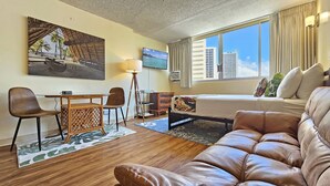A hotel room with a bed, a sofa, a dining table with chairs, a TV, and a large window with a city view. - Calm, Quiet, New, & Clean Waikiki Queen Bed Studio - WAIKIKI GRAND HOTEL® 804 (Honolulu)