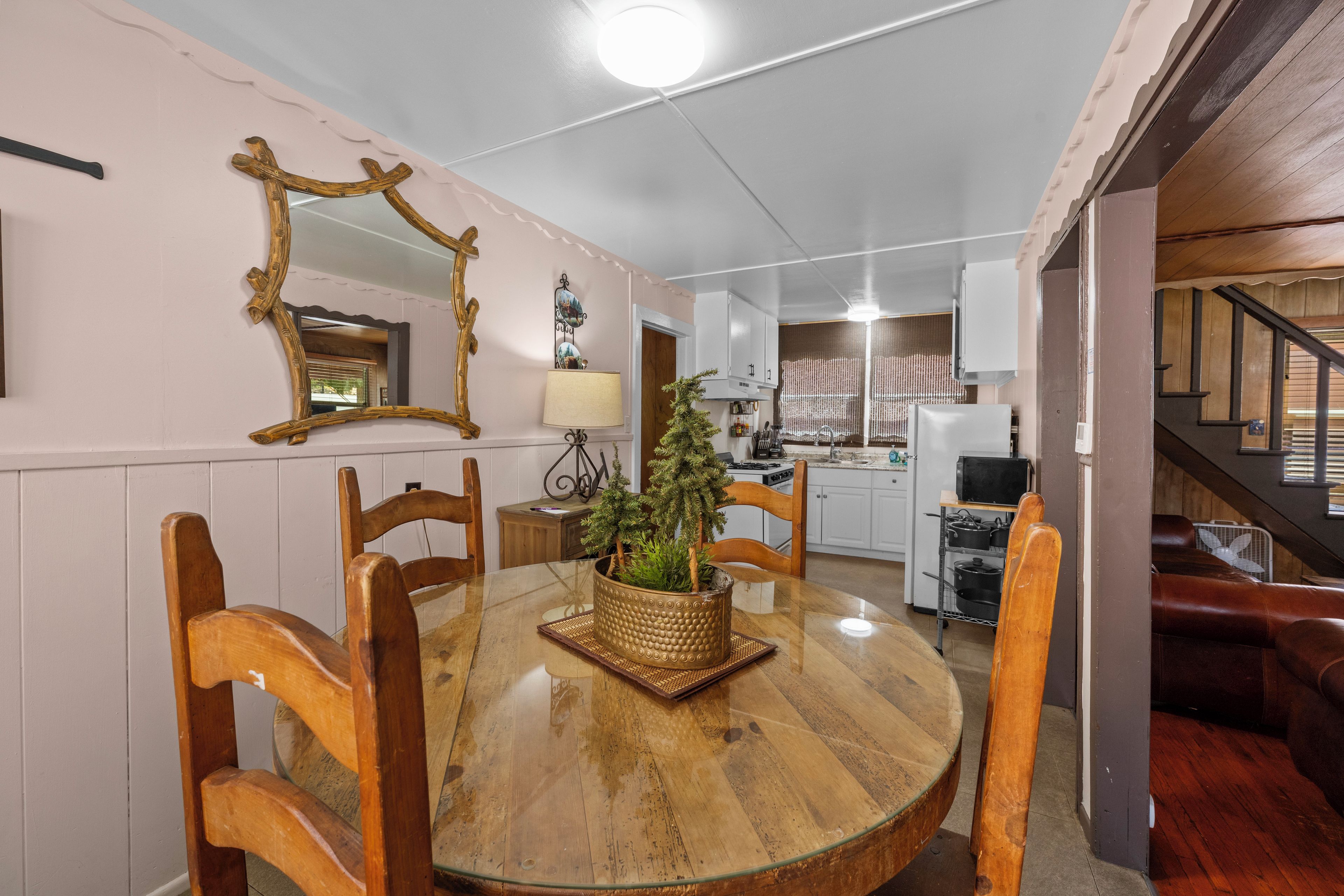 A dining area with a round wooden table, chairs, a potted plant, and a mirror on the wall.