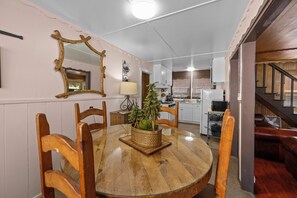 A dining area with a round wooden table, chairs, a potted plant, and a mirror on the wall. - Lake Cottage (Big Bear Lake)