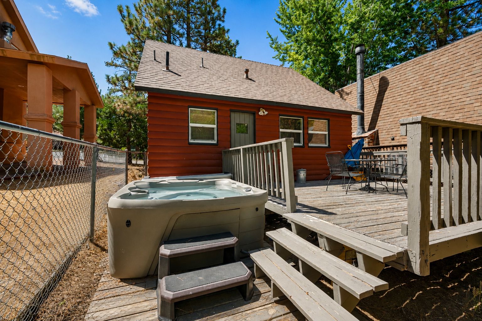 Une terrasse en bois avec un jacuzzi, des marches et une zone délimitée par une clôture.