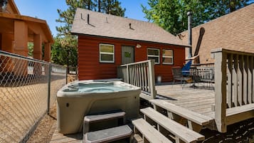 A wooden deck with a hot tub, steps, and a fenced area.