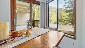 Een eetgedeelte met een houten tafel, kaarsen en uitzicht op een bergachtig landschap door grote ramen.