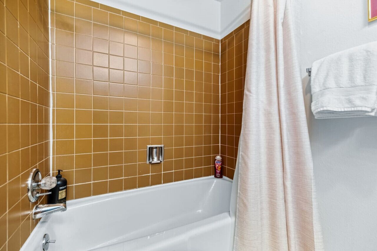 Een badkamer met een witte badkuip, bruine betegelde muren, een witte handdoek en een fles shampoo.