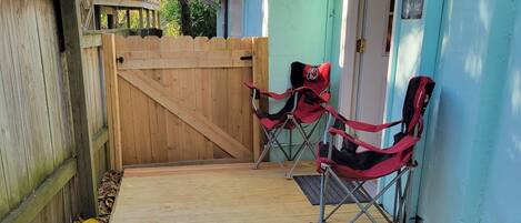 A wooden deck with two red folding chairs, a wooden gate, and a stone pathway.