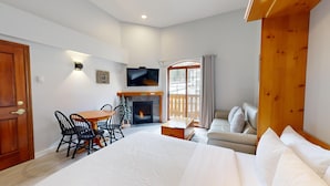 Ein modernes Schlafzimmer mit einem großen Bett, einem Holztisch, einem Kamin, einem Fernseher und einem Balkon mit Vorhängen.