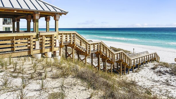 A beach house with a wooden deck and stairs leading to a covered area overlooking the ocean. - Amalfi Coast B219 * Scenic 98 near restaurants * Salt Water Vacations (Destin)