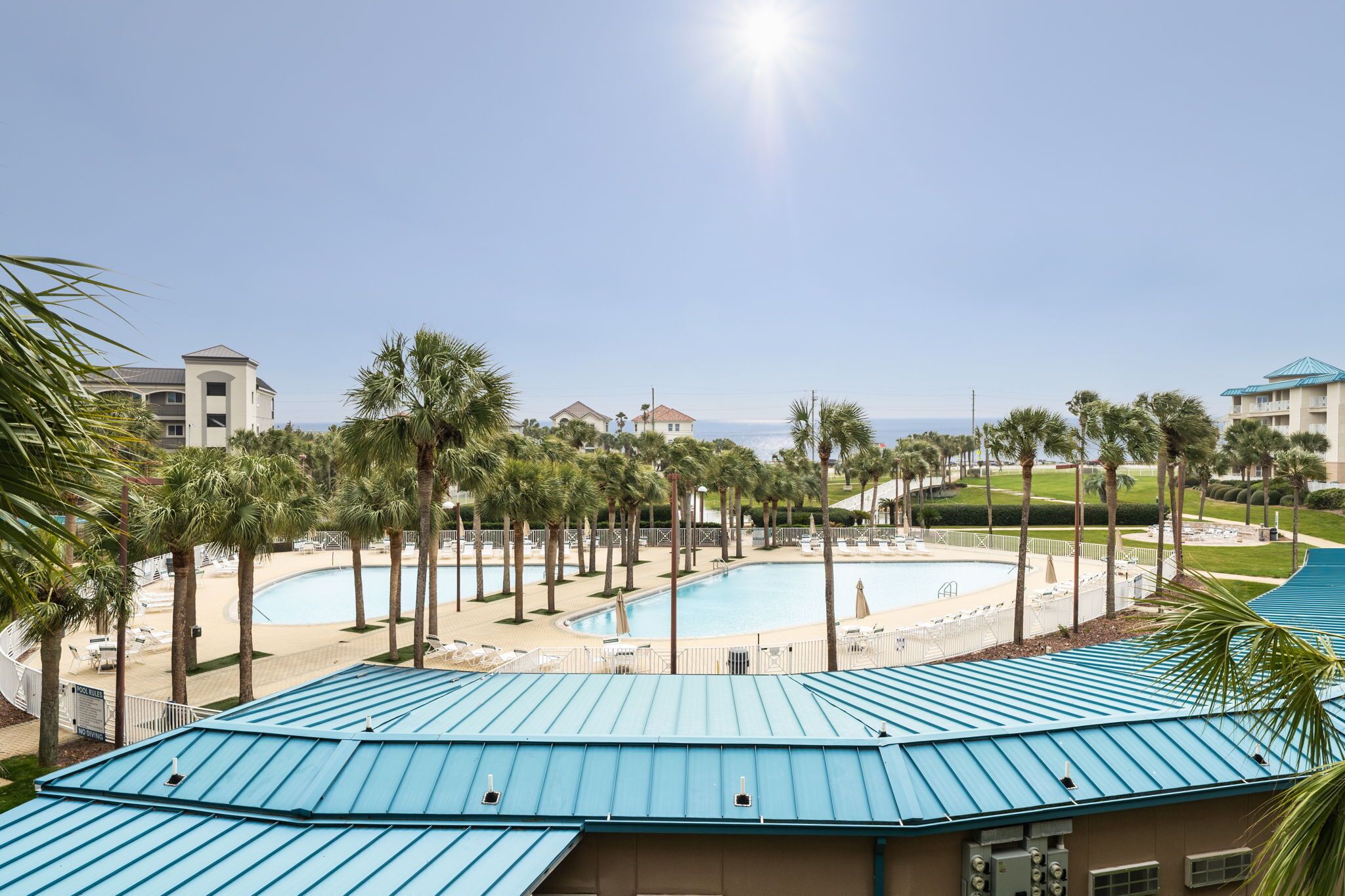 A resort with a large pool, palm trees, and a clear view of the ocean.