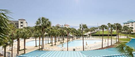 A resort with a large pool, palm trees, and a clear view of the ocean.