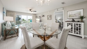 A dining area with a glass table surrounded by cushioned chairs, a chandelier, and a view of the outdoors. - Amalfi Coast B219 * Scenic 98 near restaurants * Salt Water Vacations (Destin)