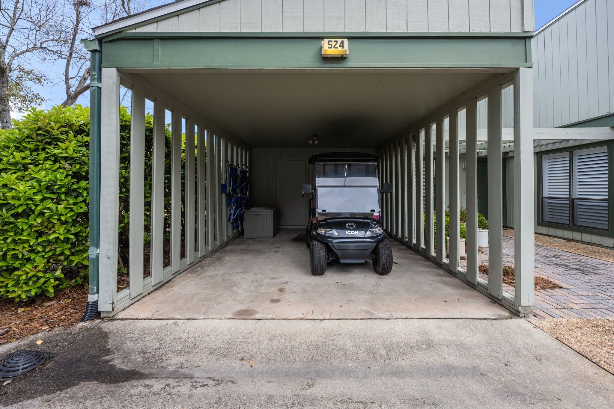 Een overdekte parkeerplaats met een voertuig erin, een bord met nummer 524 erboven en een groene haag aan de linkerkant.