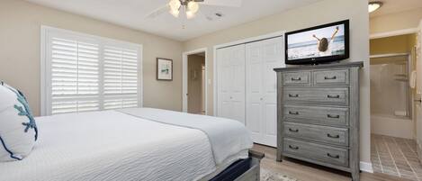 Un dormitorio con cama, ventilador de techo, televisor, cómoda y vestidor.