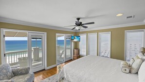 Ein Schlafzimmer mit einem großen Bett, einem Deckenventilator und Blick auf den Strand durch Glastüren.