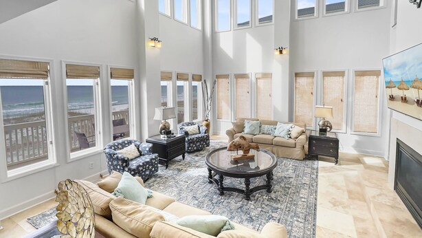 Ein geräumiges Wohnzimmer mit großem Fenster zum Meer, ein beiges Sofa, ein Couchtisch und ein Kamin.