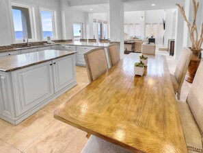 A spacious kitchen with a large island, a dining area with a wooden table, and a living room with a sofa and decorative plants.