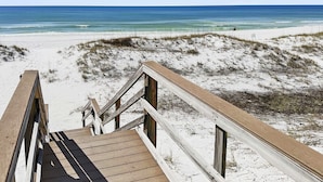 Ein hölzerner Steg führt zu einem Strand mit Dünen und dem Meer im Hintergrund.