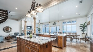 A spacious kitchen with marble countertops, wooden cabinets, and a large island. There are pendant lights, a ceiling fan, and large windows offering views. - Gulf Paradise * Golf Cart & Beach Chair Set * Gulf Front * Salt Water Vacations (Miramar Beach)