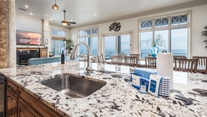A spacious kitchen with a large granite countertop, a stainless steel sink, and a view of the ocean through large windows. - Gulf Paradise * Golf Cart & Beach Chair Set * Gulf Front * Salt Water Vacations (Miramar Beach)