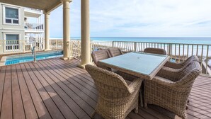 A wooden deck with a glass-top table and wicker chairs, overlooking a beach and ocean. - Gulf Paradise * Golf Cart & Beach Chair Set * Gulf Front * Salt Water Vacations (Miramar Beach)