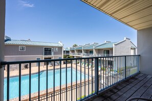 A pool area with a view of a building with multiple balconies and a clear blue sky.
