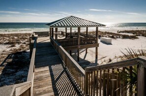 A wooden boardwalk leading to a beach gazebo with a metal roof.