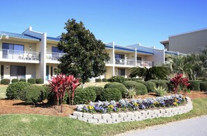 A multi-story hotel with balconies, a landscaped garden with various plants, and a clear blue sky.