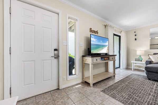 A living room with a television on a wooden stand, a door with a view of the outside, and a wall-mounted sign that says "Beach".