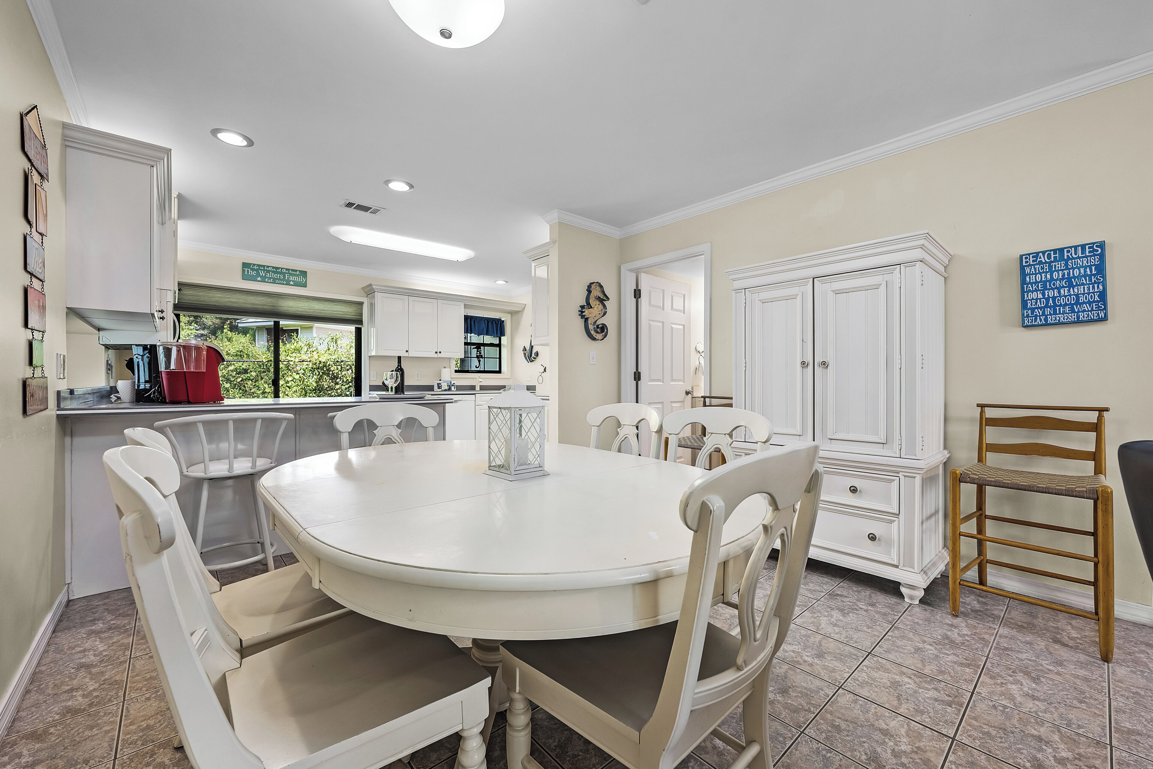 Un comedor con una mesa redonda y sillas, una cocina al fondo y un letrero en la pared.