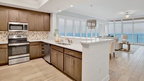 A modern kitchen with a large island, stainless steel appliances, and a view of the ocean. - Phoenix Gulf Tower 1704 | Spacious, luxurious, Newest OBA development! (Orange Beach)