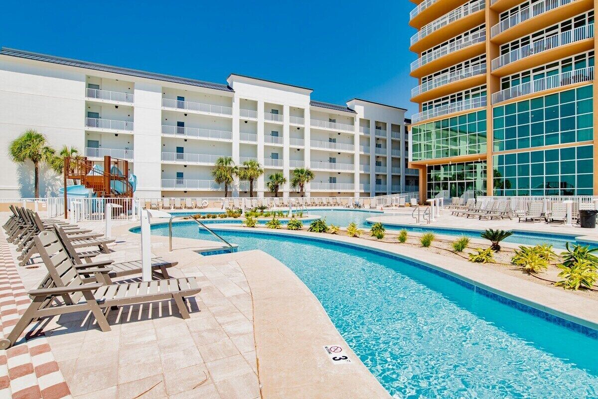 A hotel with a swimming pool, sun loungers, and a children's play area.