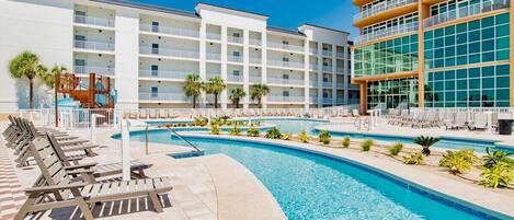 A hotel with a swimming pool, sun loungers, and a children's play area.