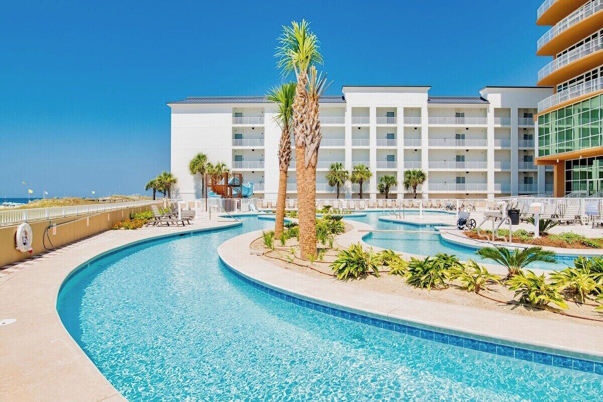 Ein Hotel mit großzügiger Poolanlage, Palmen und blauem Himmel.