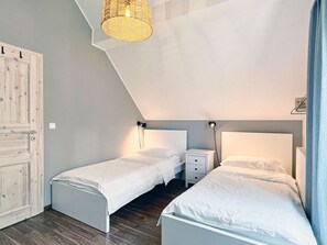A bedroom with two single beds, a wooden door, a sloped ceiling, and a hanging light fixture.