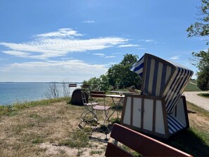 A beachside area with a view of the sea, a bench, and a small structure with a flag.