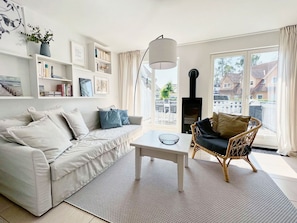 Ein Wohnzimmer mit Sofa, einem Sessel, einem Couchtisch, einem Kamin und Blick ins Freie.