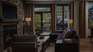 A cozy living room with a fireplace, comfortable seating, a dining area, and large windows offering a view of the outdoors. - NorthStar Lodge at Lake Tahoe in walking distance to ski lifts! (Truckee)