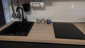 Eine Küche mit einem schwarzen Spülbecken, einem schwarzen Wasserhahn, einem Topf, der an einem Gestell hängt, einer Küchenpapierrolle und drei Gewürzbehältern mit den Aufschriften 'SALE', 'CAFFE' und 'ZUCCHERO'.