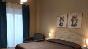 Ein Schlafzimmer mit einem großen Bett, einem Sessel, einem Nachttisch mit Lampe und zwei an der Wand befestigten Kunstwerken.