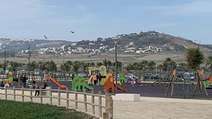 Ein Spielplatz mit verschiedenen Spielgeräten, einer gepflasterten Fläche und einer Aussicht auf eine hügelige Stadt im Hintergrund.
