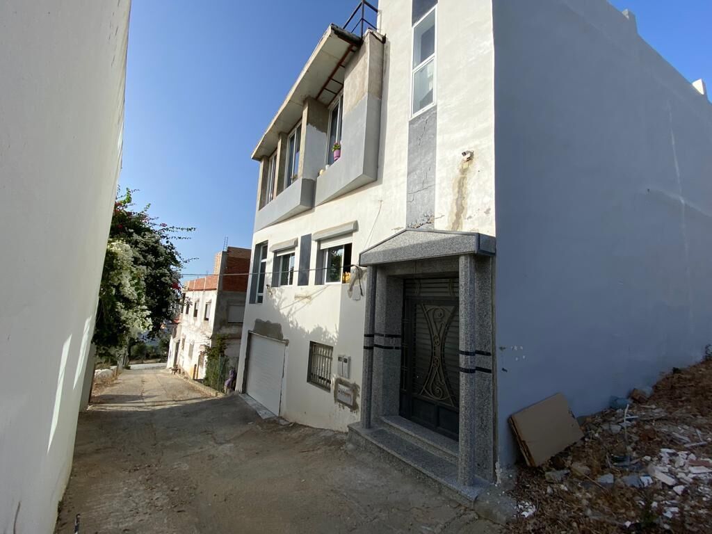 Eine schmale Straße mit einem zweistöckigen Gebäude, das ein großes Fenster und eine Tür mit schmiedeeisernen Verzierungen aufweist.