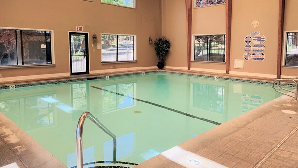 A swimming pool with clear water, surrounded by windows and a wooden ceiling. - Lakefront Viking Oasis Condo (Big Bear Lake)