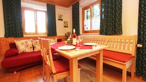 Un coin repas chaleureux avec une table en bois dressée pour deux personnes, un banc recouvert d’un tissu rouge et un canapé rouge.