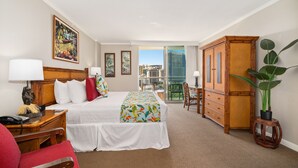 Habitación de hotel con cama, escritorio, silla, armario y balcón con vista a la ciudad.