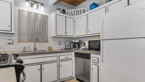 A modern kitchen with white cabinets, a stainless steel dishwasher, a coffee maker, and a kettle. - Aqua Dreams (Big Bear City)