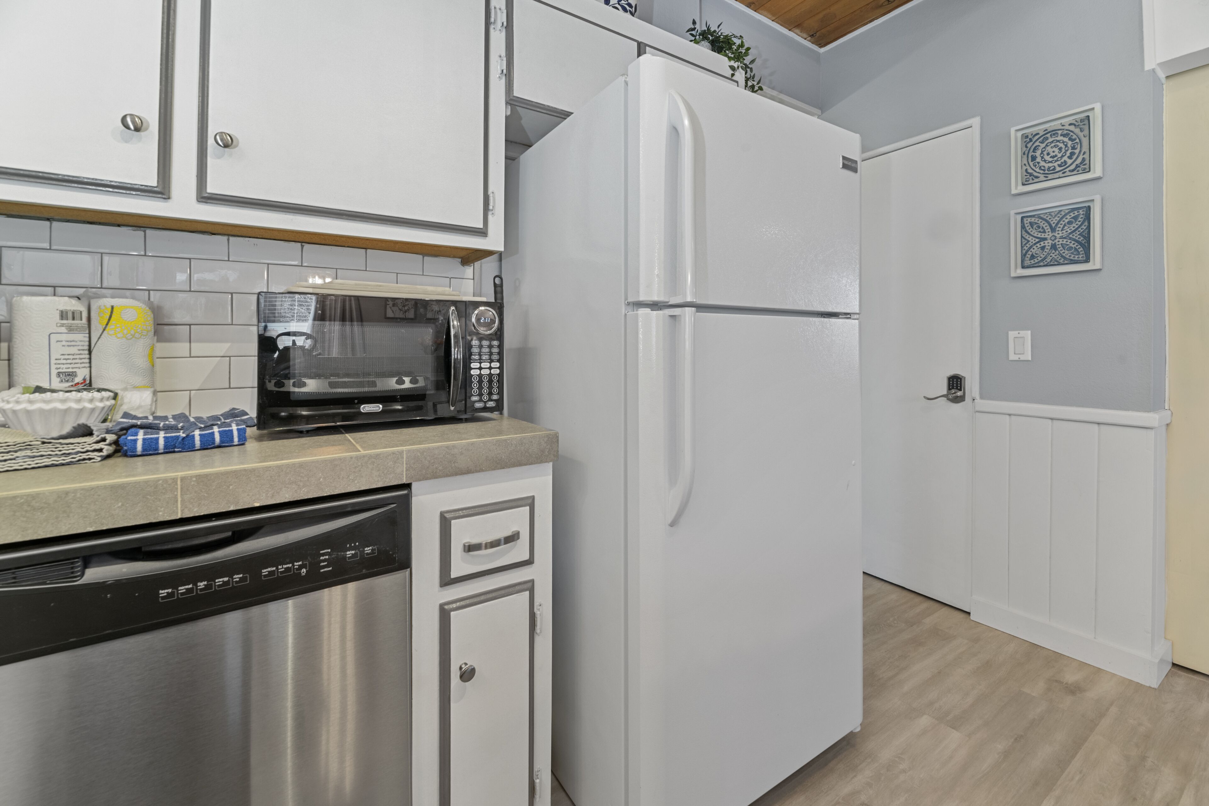 A kitchen with white cabinets, a stainless steel dishwasher, a white refrigerator, and a microwave on the countertop.