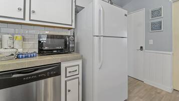 A kitchen with white cabinets, a stainless steel dishwasher, a white refrigerator, and a microwave on the countertop.