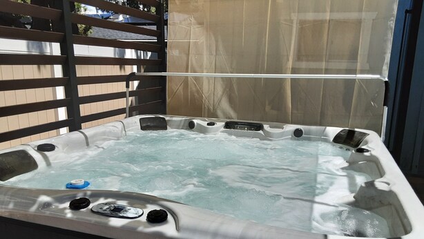 A hot tub with a wooden deck and a beige canopy. - Aqua Dreams (Big Bear City)