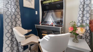 A room with a gaming arcade, a framed picture on the wall, and a vase with flowers on a table. - Aqua Dreams (Big Bear City)