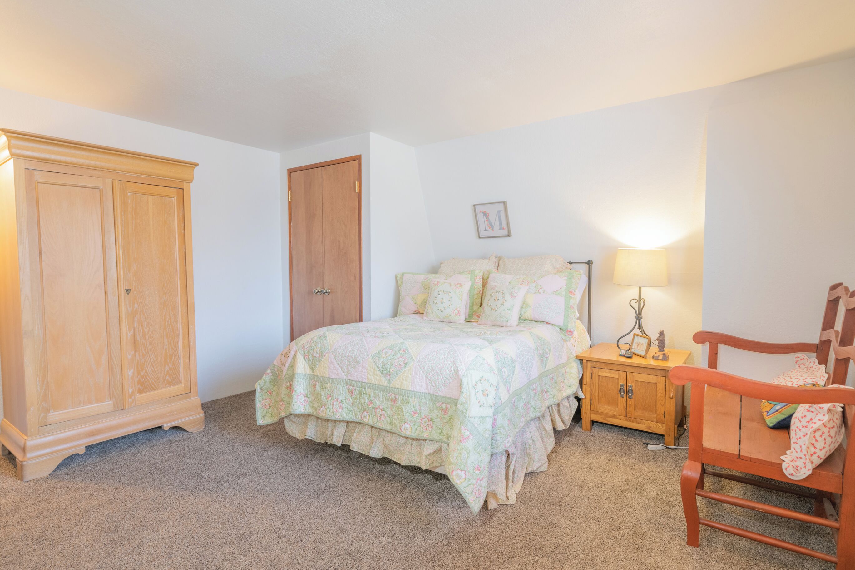 Un dormitorio con cama, armario de madera, mesita de noche y una silla.